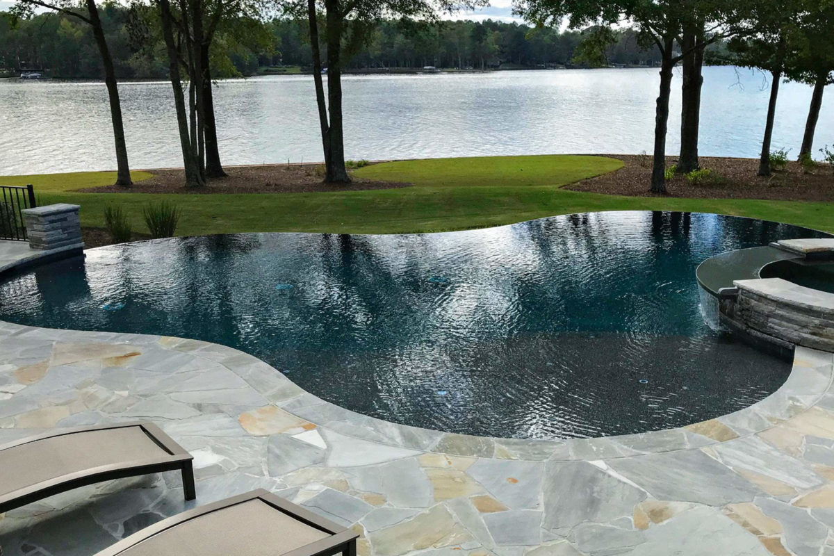 photo of a round backyard pool design in PebbleTec Black Pearl Pool Finish dark blue water color with a lakeside view