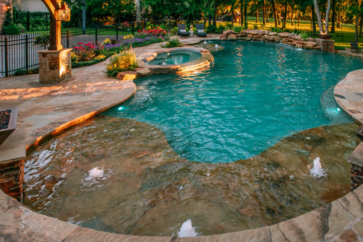 photo of a resort style backyard round pool design in PebbleTec Caribbean Blue Pool Finish medium blue water color at sunset