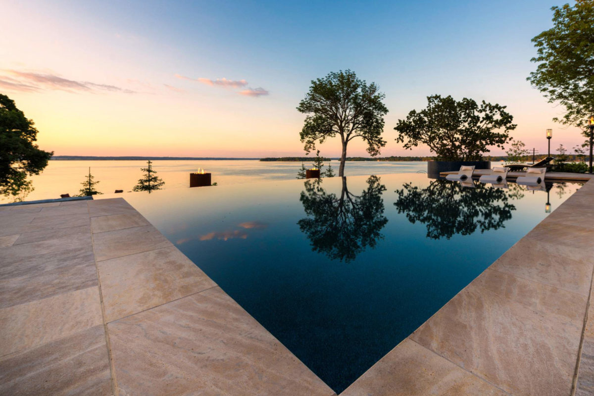 photo of a waterfall edge pool in PebbleTec Midnight Blue Pool Finish medium blue water color in the evening with a sunset view over the water