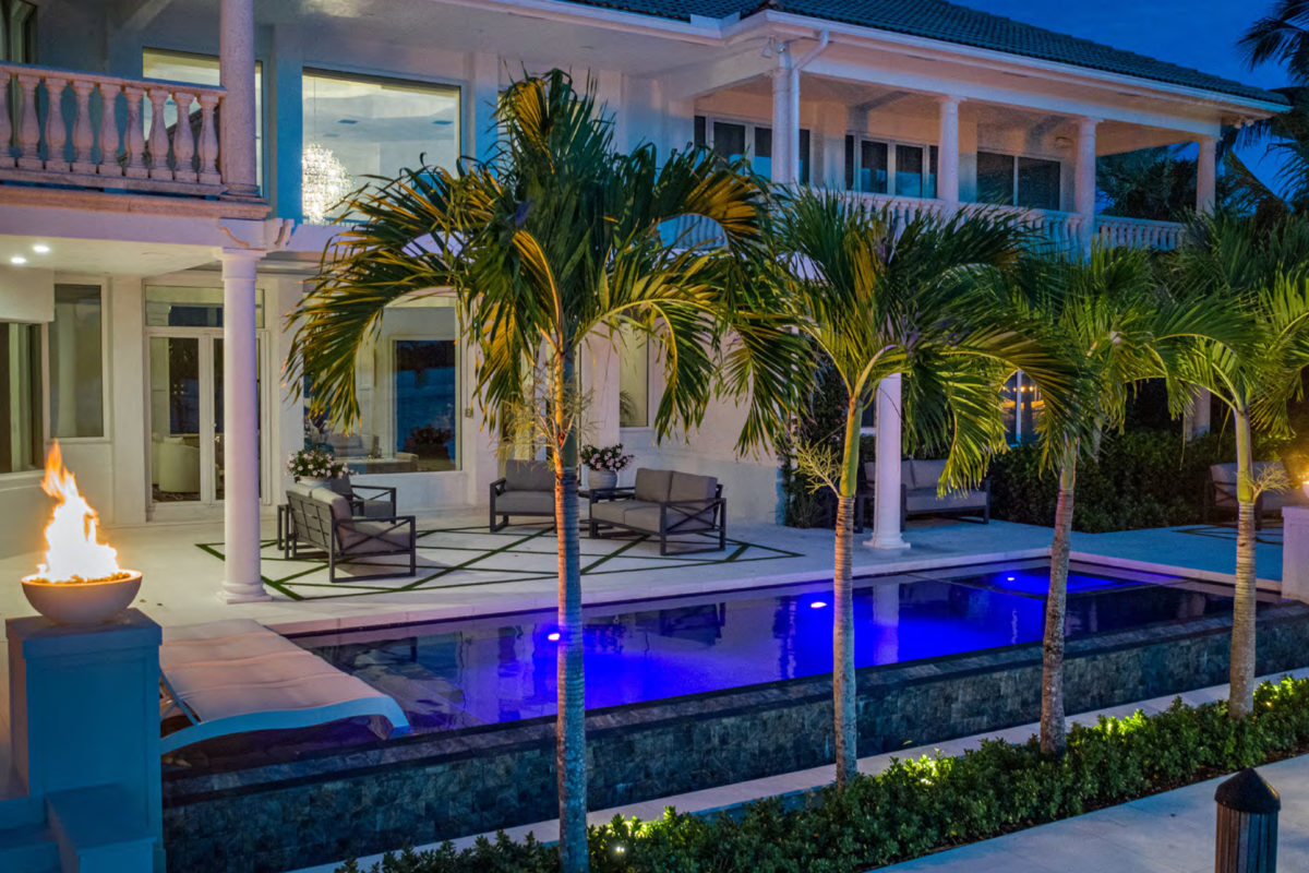 photo of a backyard pool design in PebbleTec Midnight Blue Pool Finish in the evening with a fire bowl feature and palm trees