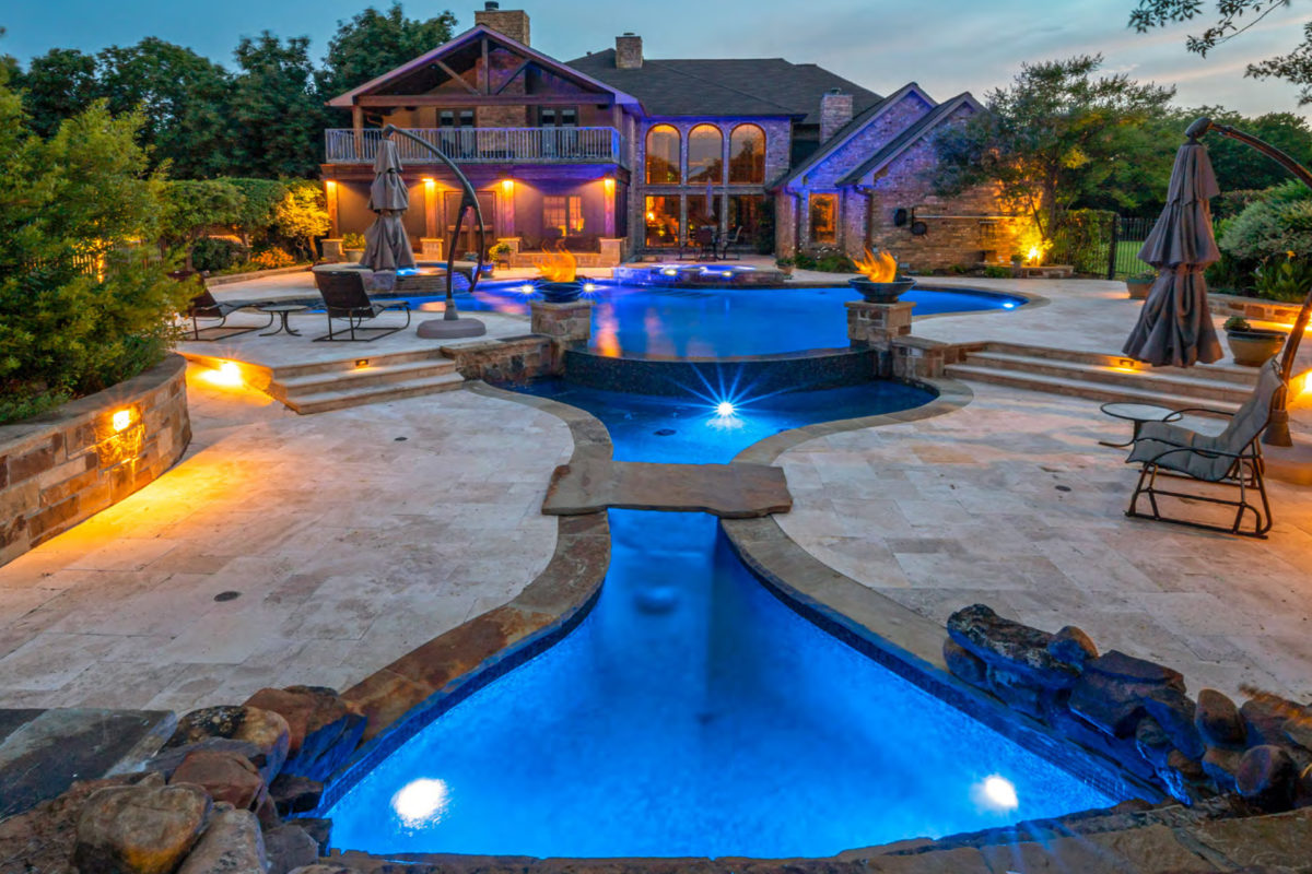 photo of unique hourglass shaped pool in PebbleTec Midnight Blue Pool Finish medium blue water color in the evening with fire bowl features