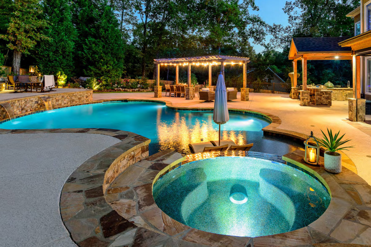 photo of a round backyard pool design in PebbleTec Midnight Blue Pool Finish in the evening with a gazebo