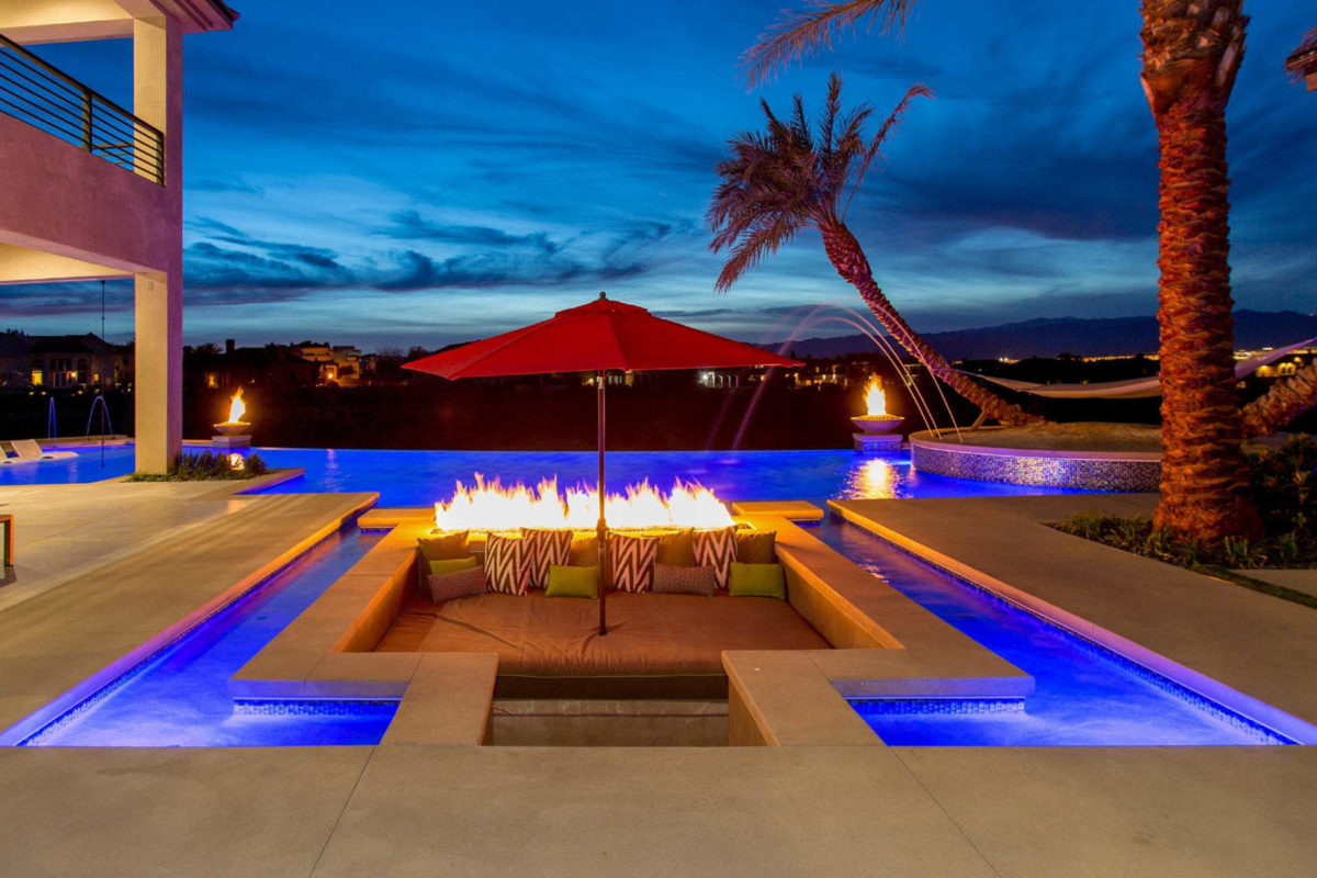 photo of a large evening lit pool with water features and fire bowls in PebbleTec Moonlight Grey Pool Finish in medium blue for World's Greatest Pools 2017