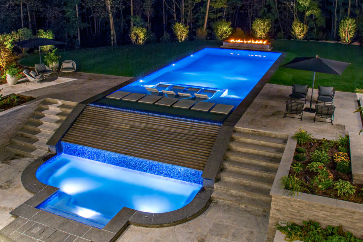photo of a large backyard pool design and fire pit in PebbleTec Moonlight Grey Pool Finish medium blue water color with a waterfall step water feature for World's Greatest Pools 2019