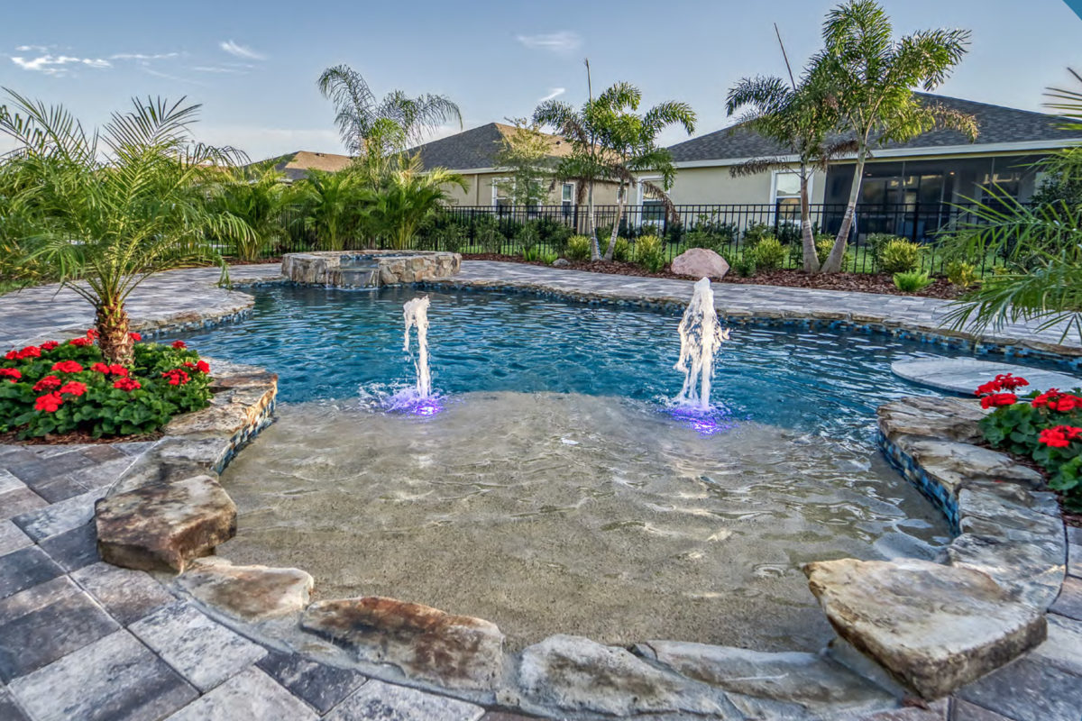 photo of a tropical backyard pool design with a round pool in PebbleTec Tahoe Blue Pool Finish medium blue water color with two lightstreams tile water features