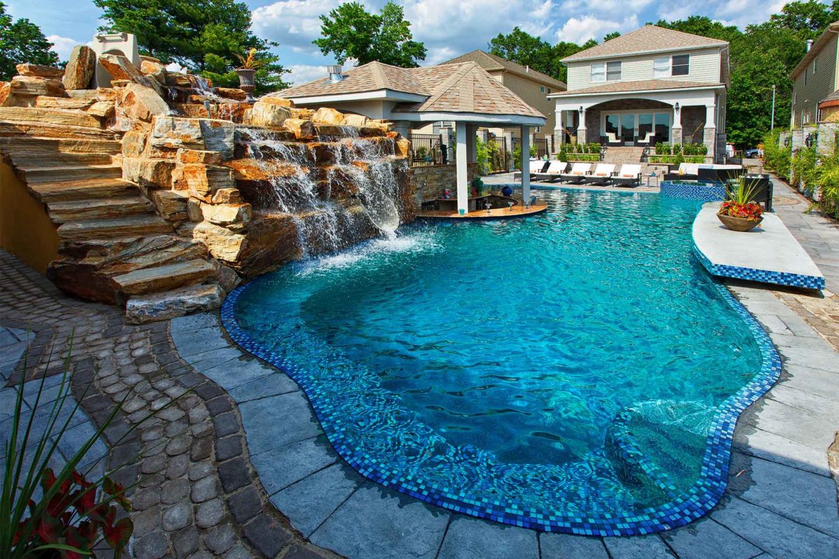 photo of a backyard pool design with a rock waterfall feature and PebbleBreeze Silver Sea Pool Finish water color by Pool Doctor